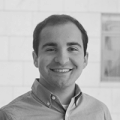 A young man wearing a button up smiles at the camera.